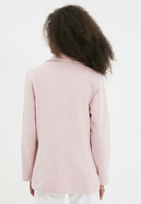 Blazer rose clair, en tissu texturé, design à un bouton, col à rabat, manches longues, dos droit et détails de couture subtils.