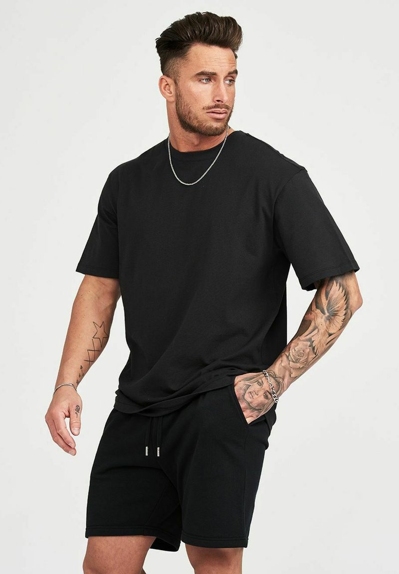 Svart bomullst-shirt med avslappnad passform, korta ärmar, parat med matchande svarta shorts. Har en mjuk textur och minimalistisk design.