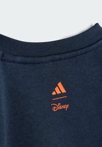 Jūras spēku pelēkā džempera apkakle ar oranžu Adidas logotipu un Disney tekstu. Izgatavots no mīksta kokvilnas auduma ar teksturētu adījuma apdari.