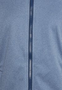 Blaue Jacke mit Reißverschluss aus strukturiertem Stoff, mit einem kontrastierenden marineblauen Reißverschluss in der Mitte. Glatte Oberfläche ohne sichtbare Muster.