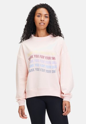 Sweat à capuche rose clair avec manches longues, col rond, et motif de texte dans des couleurs pastel variées. Texture de tissu lisse, design à coupe ample.