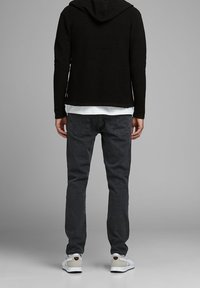 Černá mikina s texturou, vrstvená přes bílé tričko, doplněná tmavě šedými džínami a bílými teniskami s červenými detaily.