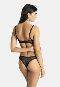 Ensemble de lingerie noire comprenant un soutien-gorge en mesh transparent avec des bretelles réglables et un string assorti avec un motif ondulé et des finitions élastiques.