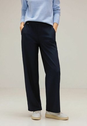 Marineblauwe wijde pantalon met verticale strepen, elastische tailleband, zijzakken en een gladde textuur, gecombineerd met lichte sneakers.