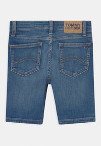 Shorts de mezclilla en azul medio con una cintura de altura media. Presentan dos bolsillos traseros y una etiqueta de cuero con "TOMMY HILFIGER" en la cinturilla.
