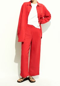 Röd skjorta med knappar som är ihop med lösa röda byxor. Vit T-shirt under. Svarta sandaler med remmar fulländar outfiten.