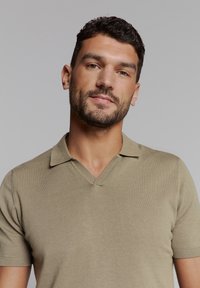 Korte mouwen, beige poloshirt met een V-hals en ribbeltextuur. Heeft een platte kraag en een aansluitend ontwerp, geschikt voor casual kleding.