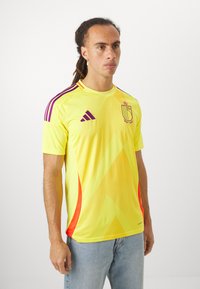 Yellow athletic jersey with purple accents and a geometric design. Features short sleeves and a crew neck. Logo displayed on the chest.