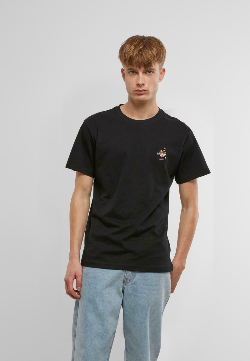 Black cotton t-shirt featuring a small, colorful cartoon design on the chest. Short sleeves, crew neckline, relaxed fit. Light denim pants.