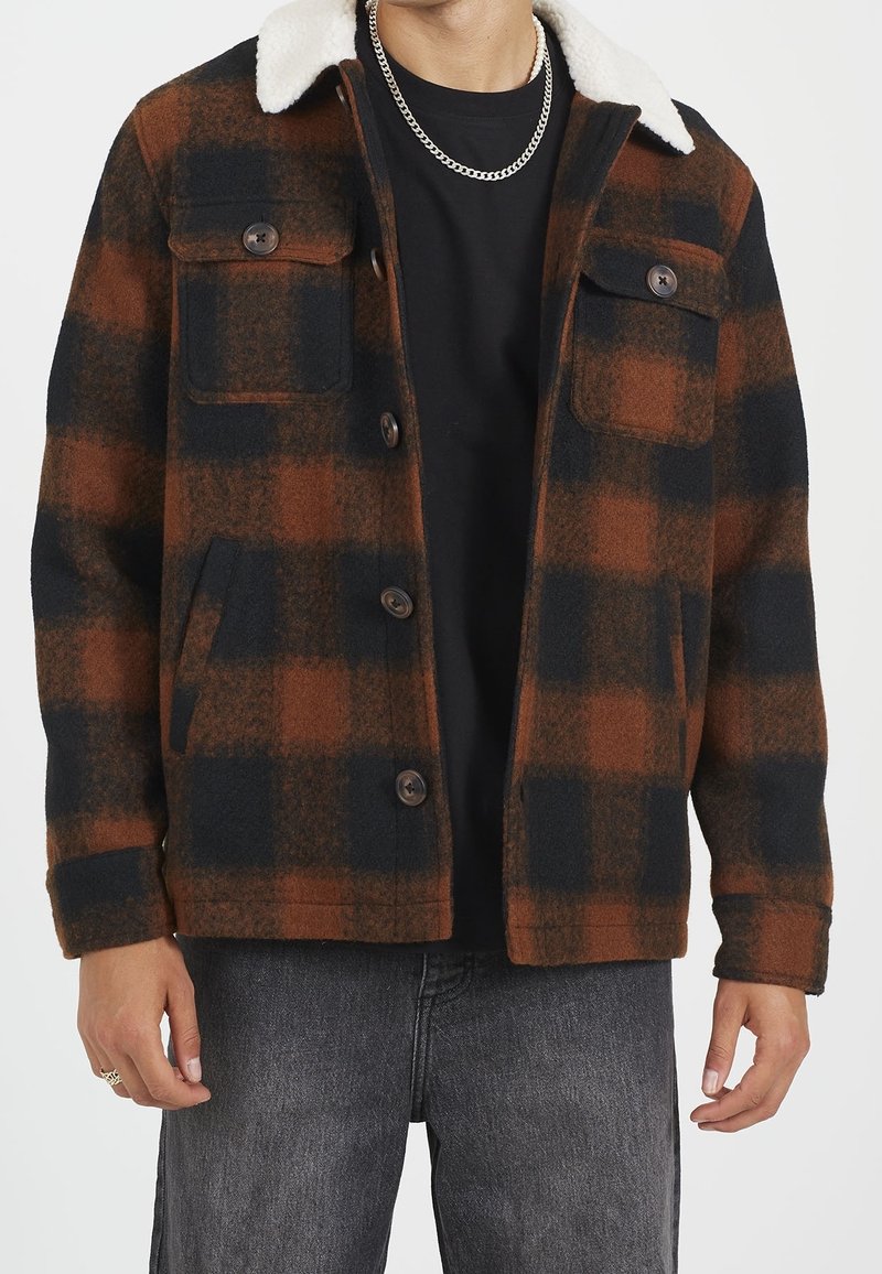 Abrigo de cuadros en marrón y negro con cuello de piel sintética blanca, con cierres de botones y dos bolsillos en el pecho. Tela suave y texturizada.