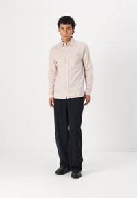 Camicia a righe rosa chiaro, con bottoni e maniche lunghe, taglio dritto; abbinata a pantaloni scuri, larghi e scarpe nere.
