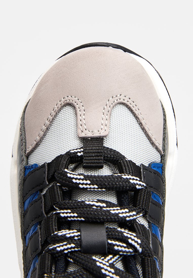 Sneaker con una toma in rete grigia, punta in suede, dettagli blu e neri, e lacci a righe bianche e nere, caratterizzata da una texture resistente.