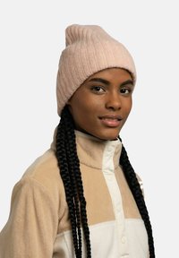 Light pink ribbed beanie with a tapered top, worn with a beige fleece jacket featuring a button-up design and cream accents.