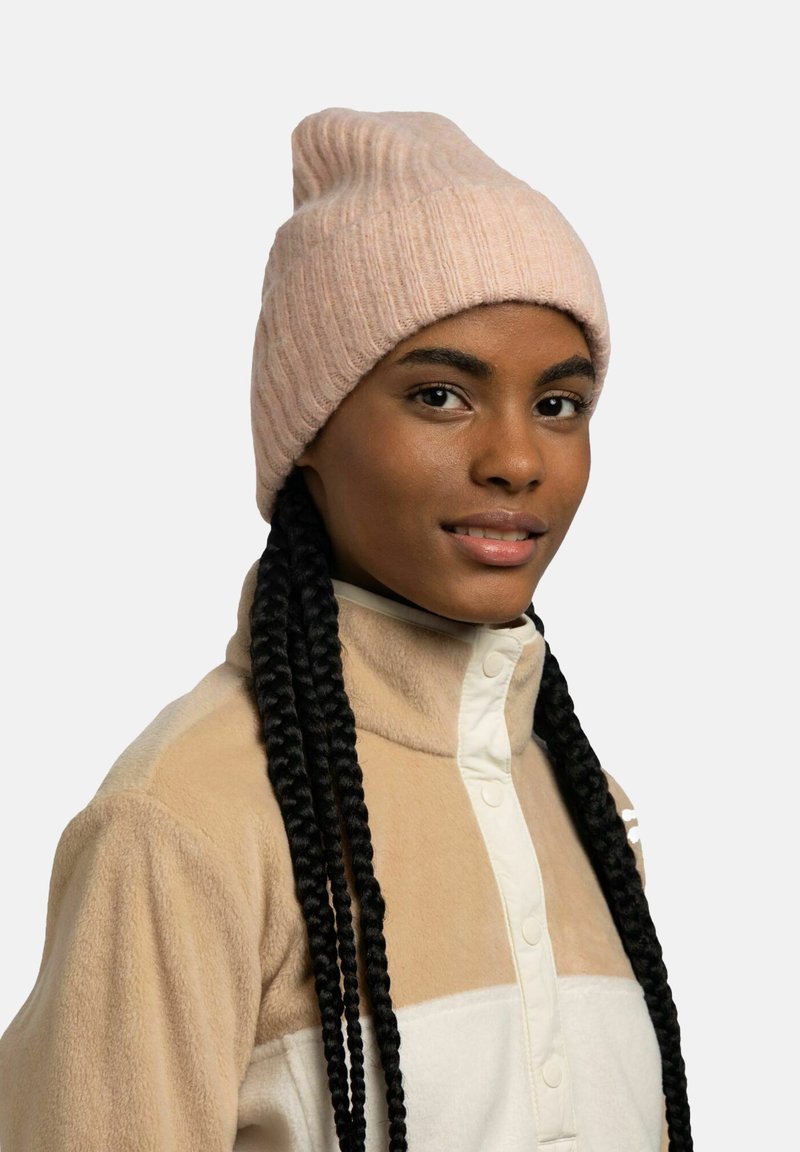 Light pink ribbed beanie with a tapered top, worn with a beige fleece jacket featuring a button-up design and cream accents.