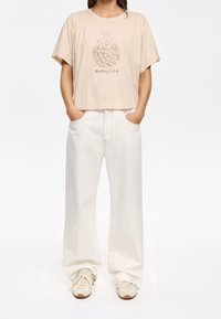 Beige cropped T-shirt with a botanical print, paired with wide white jeans and light sneakers, showcasing a relaxed fit and casual style.