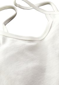 Top in tessuto morbido e bianco con scollatura rotonda e spalline sottili. Presenta una texture liscia e una leggera lucentezza, ideale per essere indossato a strati.