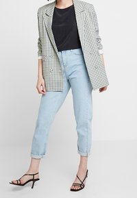 Blazer a quadri in tessuto verde e bianco, abbinato a un top nero e a jeans azzurri arrotolati. Indossato con tacchi a strappi neri.