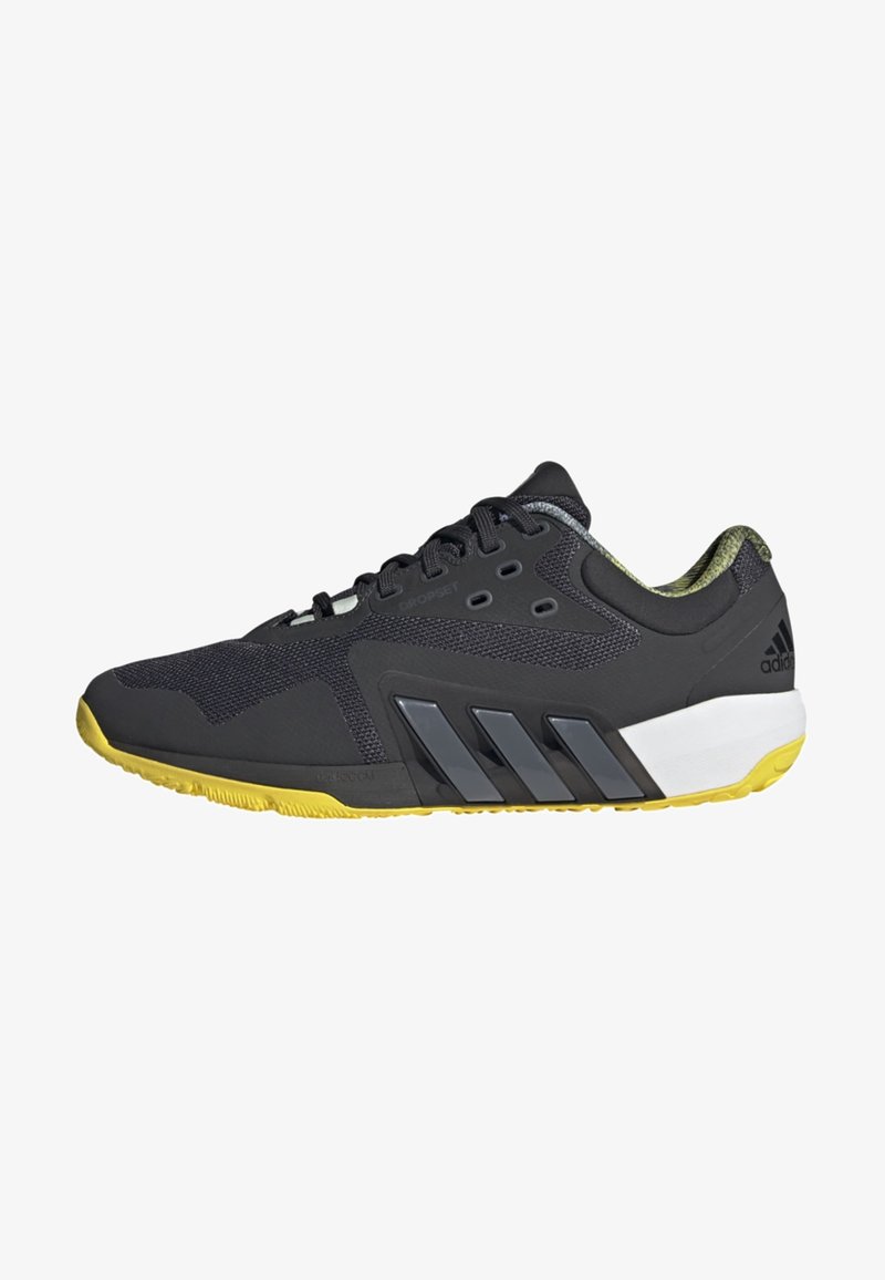 Chaussure de sport noire avec un dessus en maille et en synthétique, semelle en caoutchouc jaune, accents texturés, et trois bandes grises sur le côté.