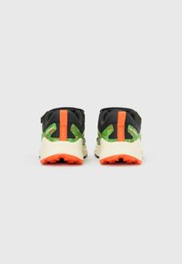 Mustade ja roheliste spordijalatsite paar, millel oranžid aktsendid ja beežid tallad, vaadatuna tagant valgel taustal.