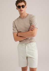 Pulover tricotat bej cu dungi, cu mâneci scurte, asortat cu pantaloni scurți de culoare deschisă cu dungi verticale și o talie elastică.