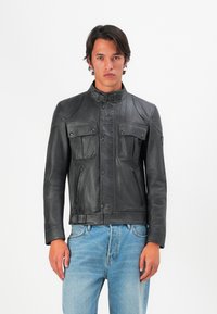 Chaqueta de cuero negra con cuello alzado, dos bolsillos en el pecho y cremalleras. Presenta un diseño de paneles y una silueta ajustada.
