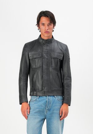 Chaqueta de cuero negra con cuello alzado, dos bolsillos en el pecho y cremalleras. Presenta un diseño de paneles y una silueta ajustada.