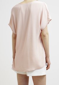 Haut rose clair, ample, en tissu doux, avec des manches courtes et un ourlet arrondi. Le dos présente un design simple et sans couture.