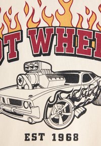 Graafinen T-paita, jossa on klassinen auto, jossa on iso pakosarjat, liekkikuvio ja rohkea "HOT WHEELS" -teksti punaisena, neutraalilla kerma taustalla.