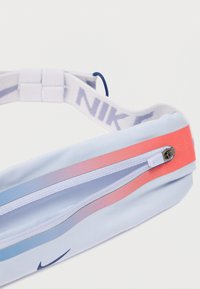 Nike bæltepose i lyseblåt stof med lyserøde og lilla striber, med en lynlåslomme og en justerbar hvid rem med logo.