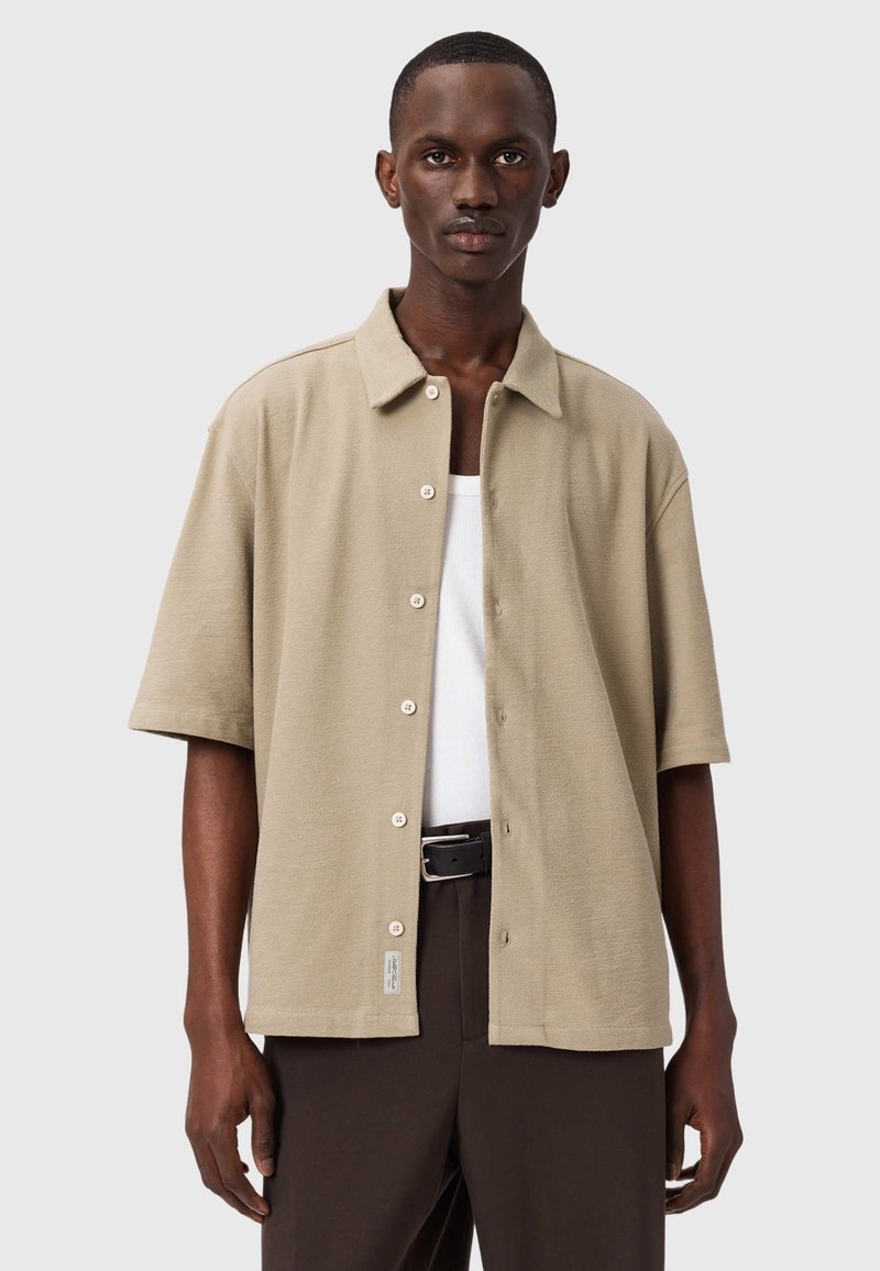 Beige overhemd met korte mouwen en knopen aan de voorkant, gemaakt van gestructureerde stof. Heeft een klassieke kraag en een klein merkembleem aan de zoom.