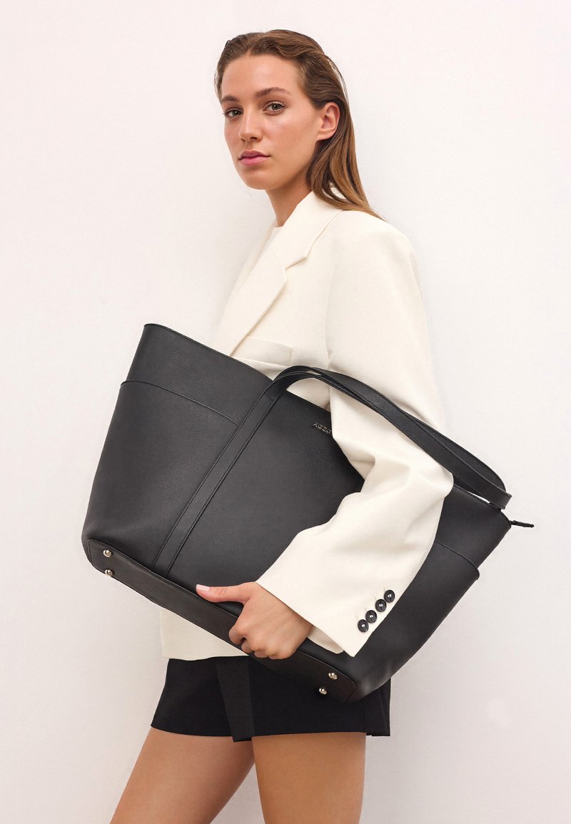 Fekete bőr bevásárlótáska strukturált formával, texturált panelek felhasználásával és levehető pánttal. Ezüst színű kiegészítőkkel rendelkezik.