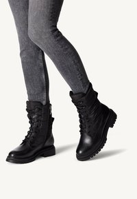Black leather ankle boots with lace-up front, padded collar, and side zipper. Features a textured sole for grip and a smooth finish.