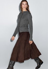 Gray ribbed cardigan with a high collar, paired with a brown suede maxi skirt, and black knee-high boots. Features a fitted silhouette.