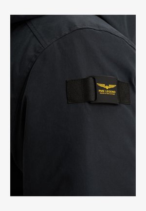 Black fabric jacket with a textured surface, featuring a prominent PME Legend label on the left shoulder and a stitched seam detail.