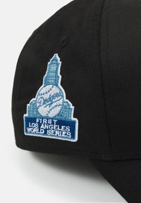 Schwarze Baseballkappe mit einem blauen und weißen gestickten Patch mit "Dodgers", einem Baseball und einem Turm, beschriftet mit "Erste Los Angeles World Series."