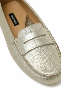 Mocassins argent métallisé en cuir texturé, avec une semelle cousue et une bande supérieure décorative comportant deux fentes horizontales.