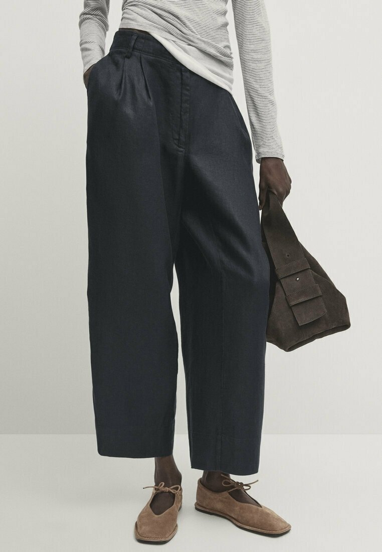 Pantalons larges marine à plis, associés à un haut ajusté à rayures à manches longues ; les accessoires comprennent un sac en daim marron foncé et des chaussures marron clair.