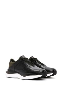 Sneakers in pelle nera con finitura texturizzata, area della punta perforata, dettagli verdi a contrasto e suola bianca imbottita.