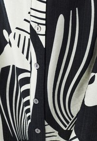 Schwarz-weißer gemusterter Hemd mit abstrakten Designs, ausgestattet mit Knöpfen an der Vorderseite und einem strukturierten Stoff.