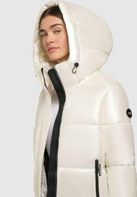 White puffer jacket with a glossy finish, featuring a large hood, black zipper, and logo accents on the sleeve and interior.