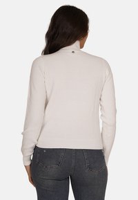 Maglione a dolcevita ribbed beige chiaro con maniche lunghe e vestibilità aderente. Presenta un piccolo logo metallico sulla parte posteriore.