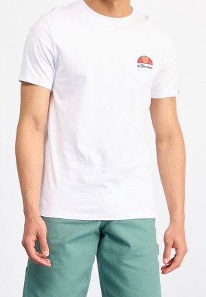 Mand iført en hvid t-shirt med korte ærmer med et orange og rødt ellesse-logo på brystet og grønne shorts.