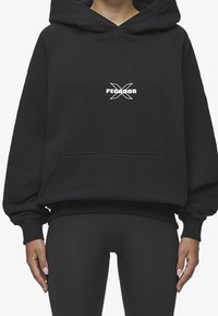 Sudadera negra de gran tamaño con un bolsillo frontal, que presenta un logo blanco de "PEGADOR" y una capucha. Fabricada con tela suave, adecuada para un uso casual.