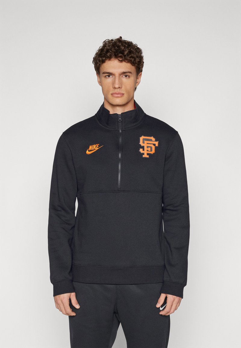 Sudadera negra de Nike con diseño de media cremallera, que presenta un logo naranja y un gráfico de SF en el pecho. Textura suave, corte estándar, manga larga.