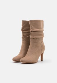 Botines de ante color beige con un diseño arrugado y una punta afilada, que cuentan con un tacón stiletto de 3 pulgadas y detalles de costura mínimos.