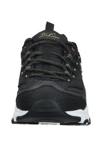 Sapatos atléticos pretos com um upper em tecido texturizado, atacadores acentuados a dourado, colarinho acolchoado e sola branca, apresentando um design de calcanhar elevado e curvado.