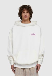 Överdimensionerad vit hoodie i mjukt tyg med en framficka och rosa logotyp på vänster bröst. Justerbar dragsko på huvan.
