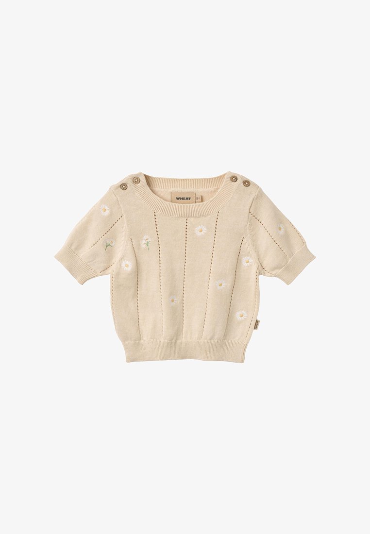 Pull bébé court à manches courtes en tricot beige avec une petite broderie de marguerite blanche, bords en côtes et détails de boutons sur l'épaule.