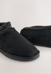 Černé pantofle s měkkým, semišovým povrchem, šedým pleteným lemem a černou gumovou podrážkou s vlnkovým vzorem.