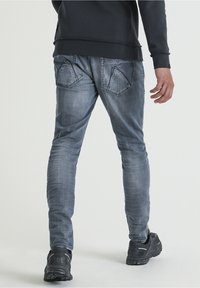 Gray denim jeans with a slim fit, featuring back yoke seams and pocket detailing. Paired with black athletic shoes.